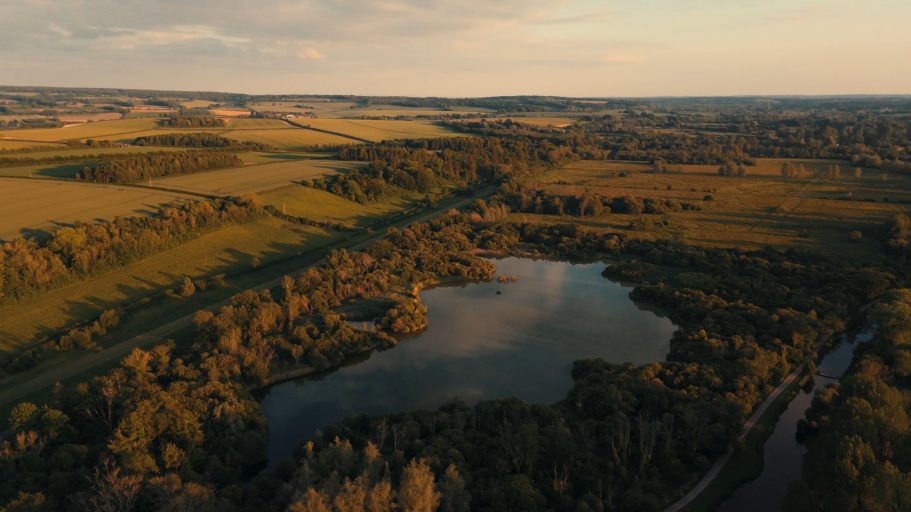 A tranquil landscape featuring a river, a lake, and lush green fields under a sunset sky.